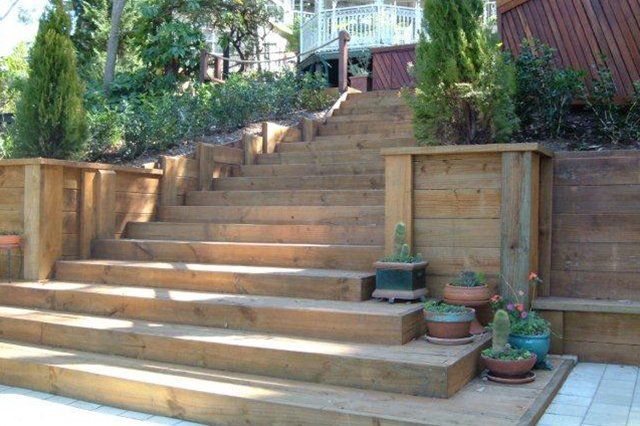 Wide stone steps leading up a landscaped garden with potted plants and wooden retaining walls