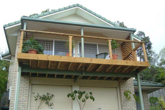 Two-story house with a large wooden balcony and potted plants under the eaves.