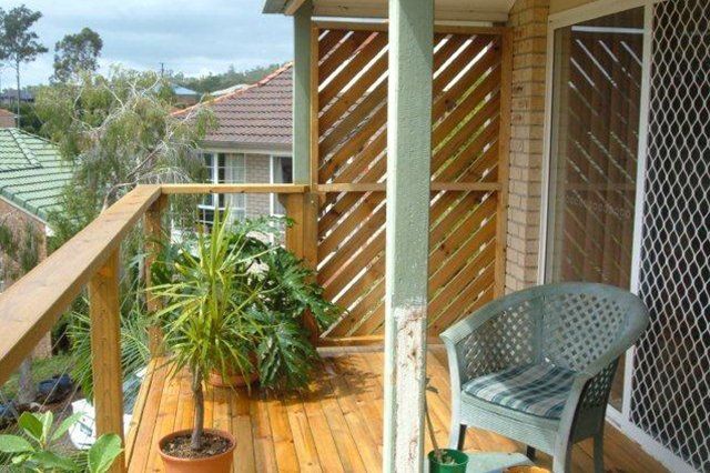 Wooden balcony with potted plants, chair, and lattice screen overlooking a neighborhood.