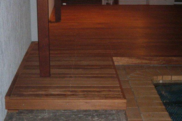 Wooden deck edge with a step down beside a tiled area and pool water