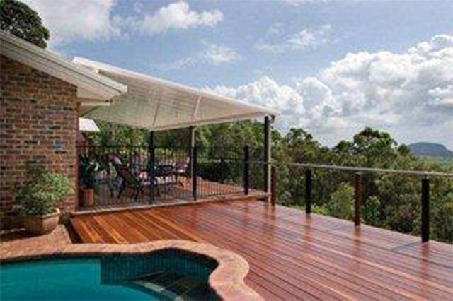 Wooden deck with pool, covered patio, and glass railing overlooking a scenic landscape