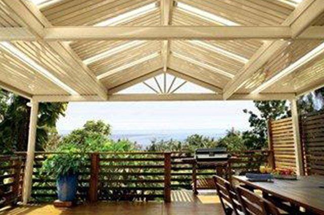 Covered wooden patio with benches overlooking a green landscape and distant ocean view