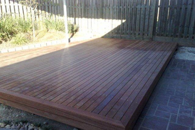 Wooden backyard deck beside a brick patio, bordered by a fence and garden area.