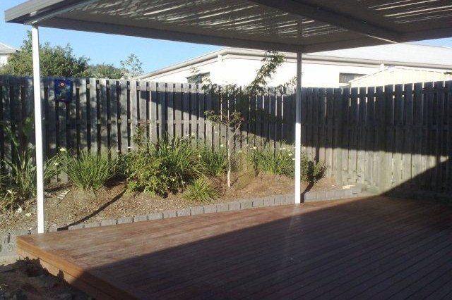 Backyard deck with wooden fence, garden bed, and covered patio roof