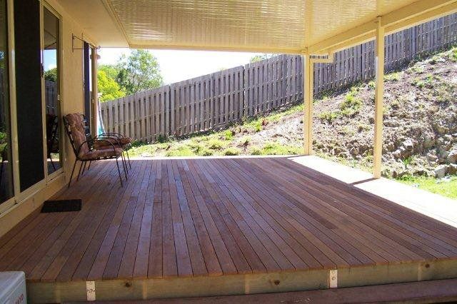 Covered wooden deck with a swing chair, railing, and grassy hillside beyond the patio.