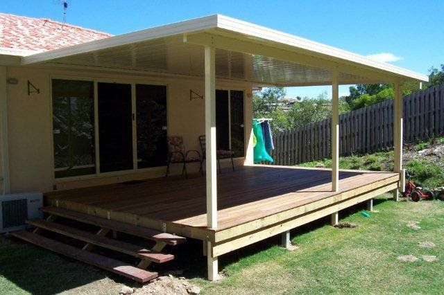 Covered wooden deck attached to a house, with steps and a fenced backyard.