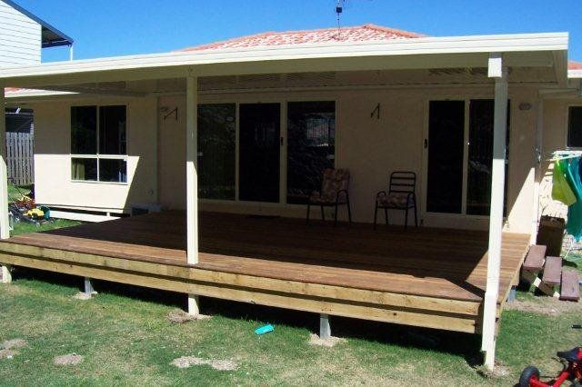 Backyard patio with a covered deck, white posts, wooden steps, and two chairs by the house