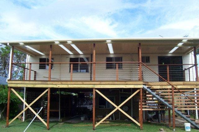 Two-story elevated wooden house with stairs, railing, and X-braced support beams in a grassy yard
