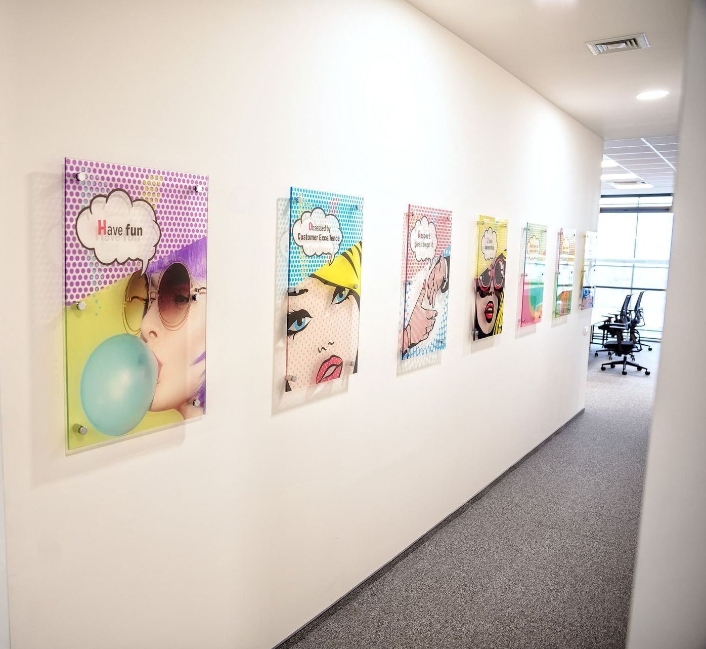 Hallway with colorful pop-art posters on a white wall, leading to an office area at the end.