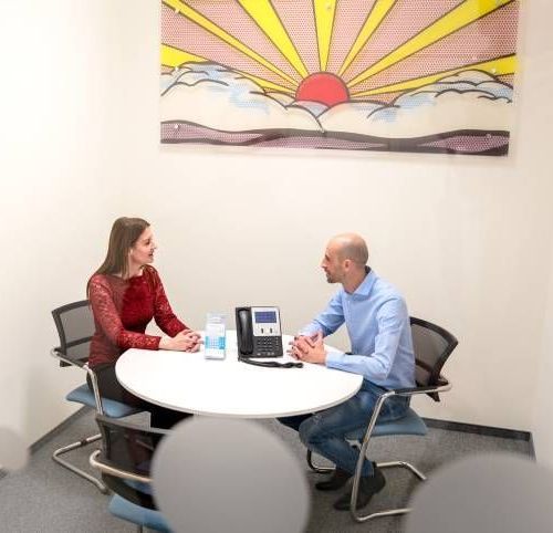 Two people talking at a small round table in a bright office meeting room
