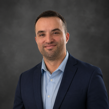 Portrait of a smiling person in a blue shirt and tie against a dark studio backdrop