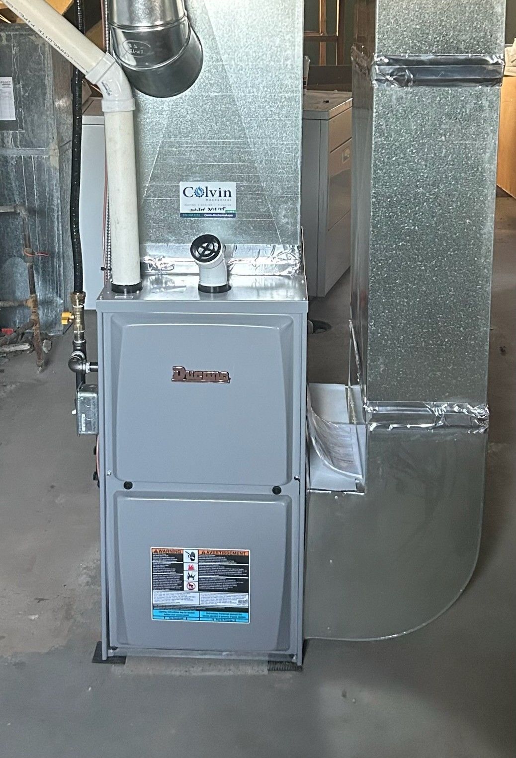 A furnace is sitting in a room next to a duct.