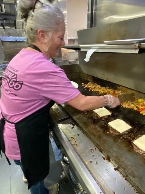 A woman in a pink shirt is cooking food on a grill.