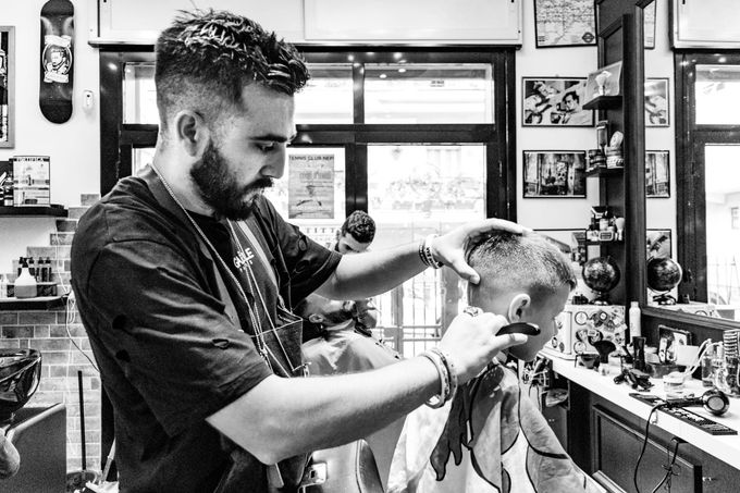 In un salone, un barbiere con la barba taglia i capelli a un cliente con le forbici, mentre un altro paio di forbici è visibile sullo sfondo.