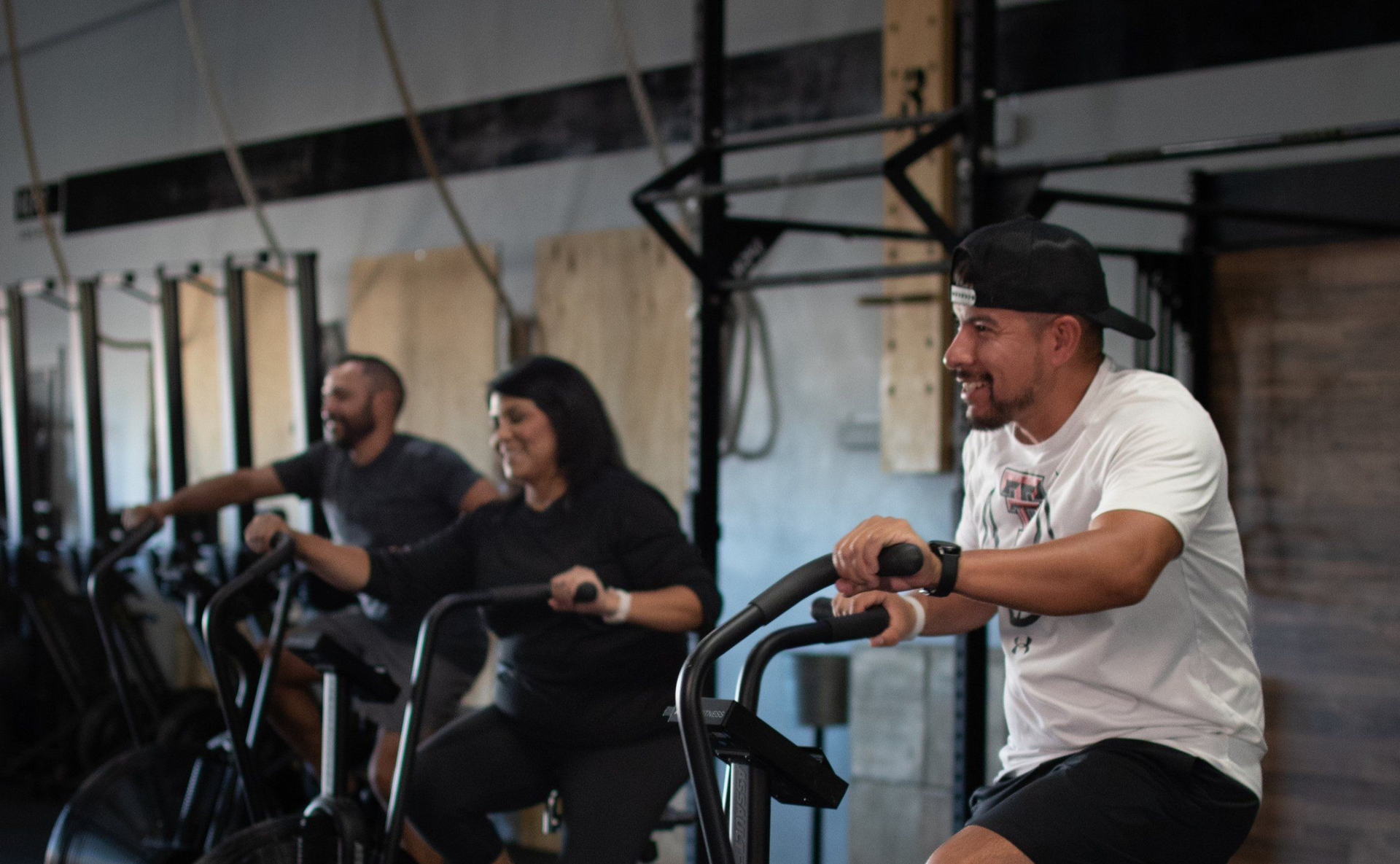 Three people smiling and exercising on stationary bikes at the gym Sweat District in Lubbock, TX.