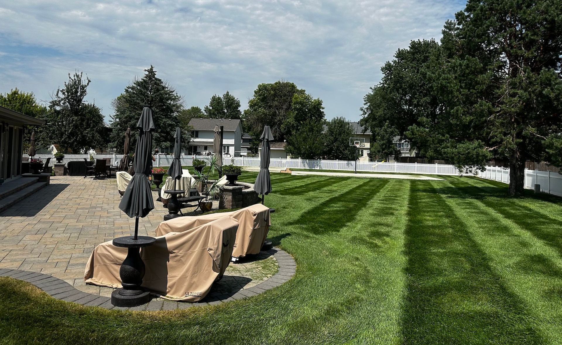 A lush green lawn with a patio and umbrellas in the background.
