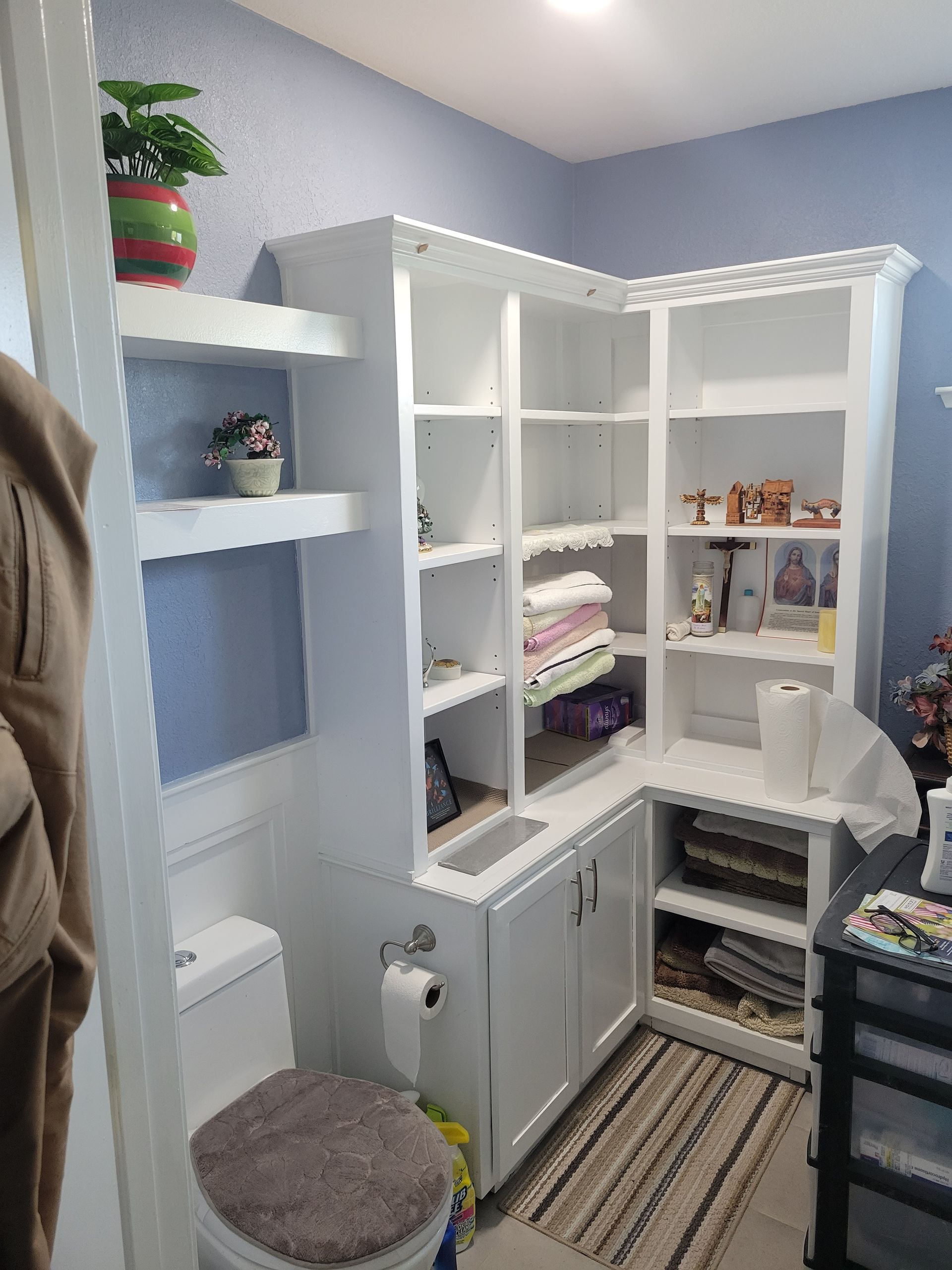 White bathroom vanity and open shelving with towels, bins, and striped rug in a small corner bathroom