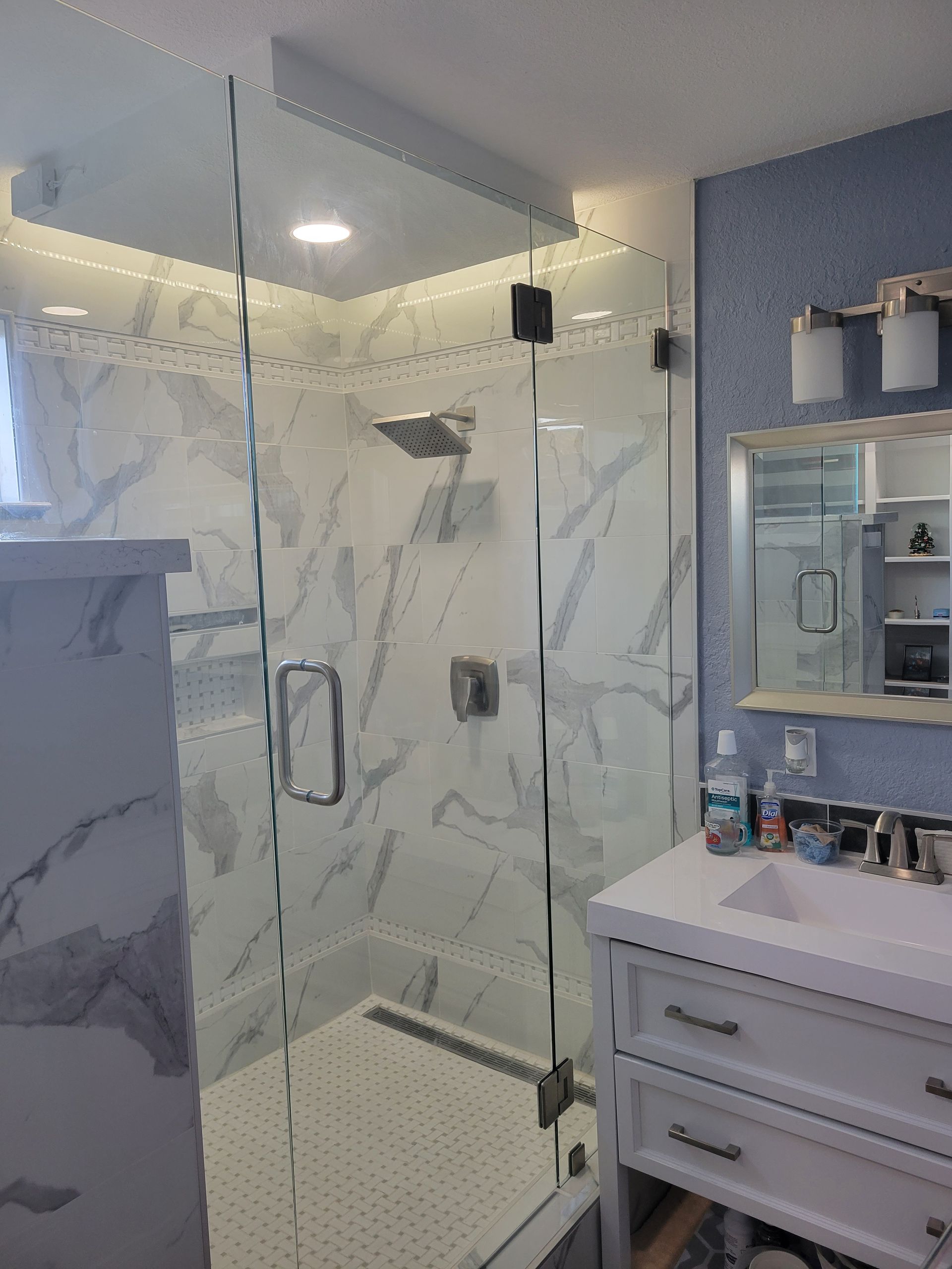 Modern bathroom with glass shower, marble-look tile, and white vanity with mirror and shelves