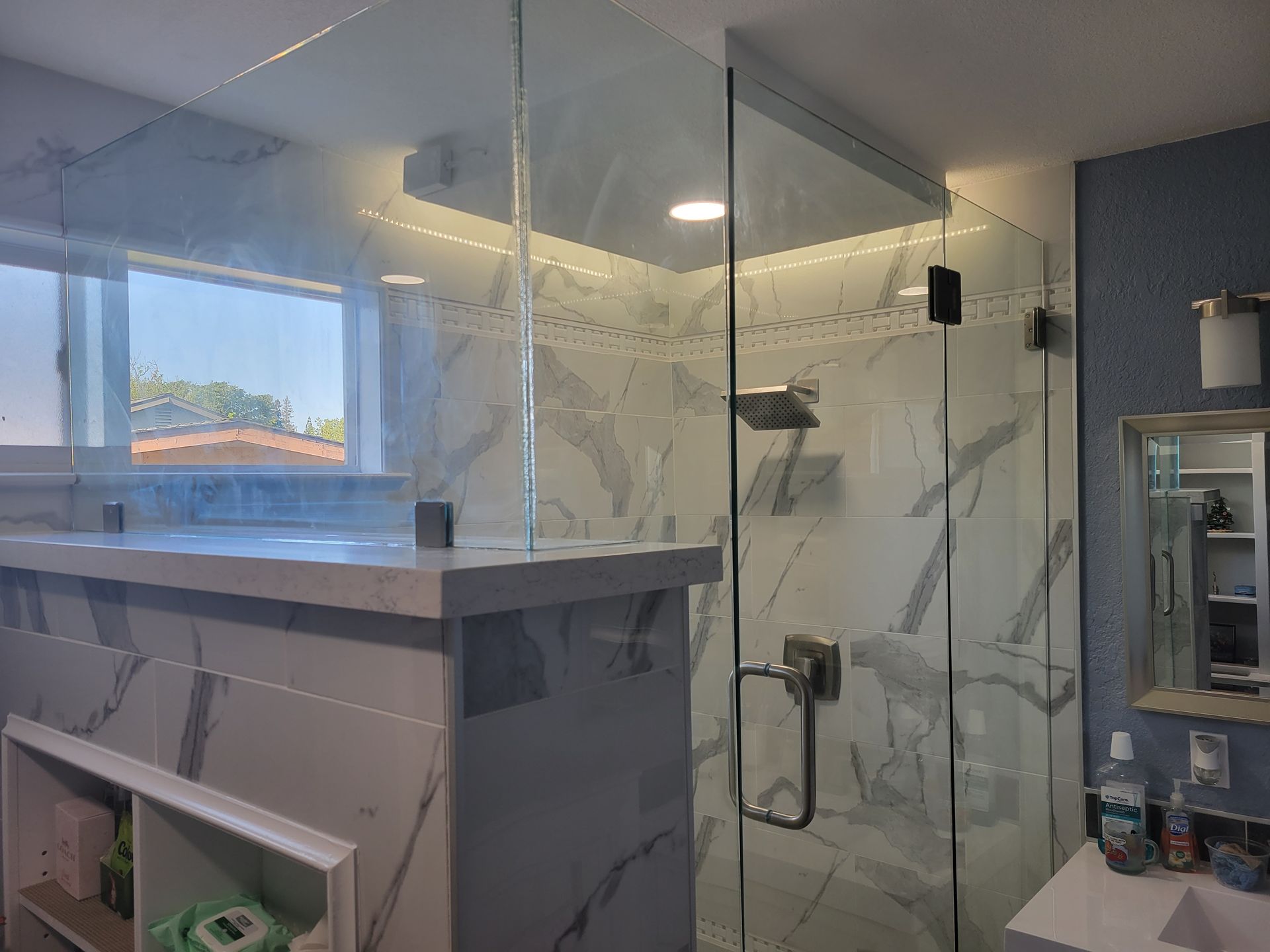 Modern bathroom with a glass shower enclosure, gray vanity, and large window overlooking a building.