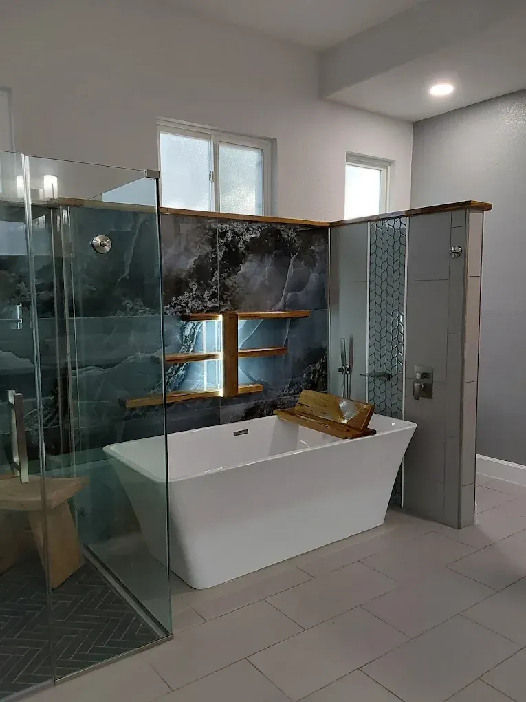 Modern bathroom with glass shower, white bathtub, and stone accent wall