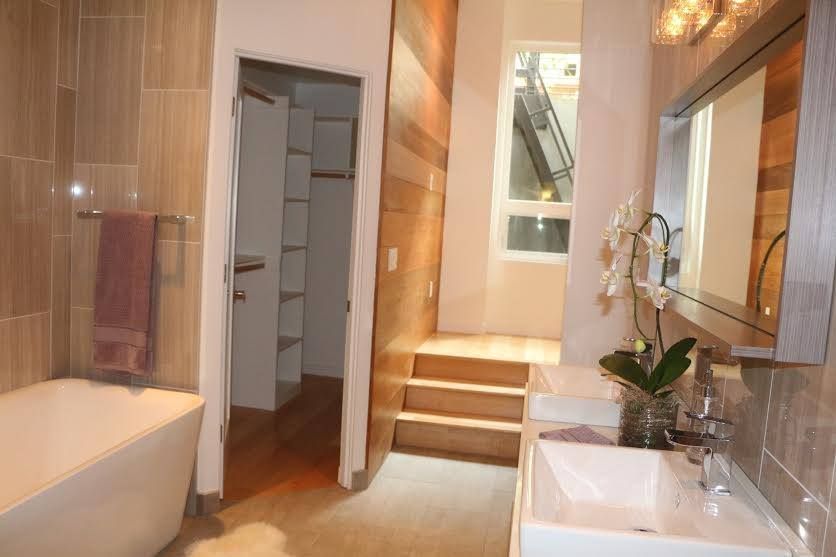 Bright bathroom with bathtub, sink, mirror, and open closet leading to a lit hallway.