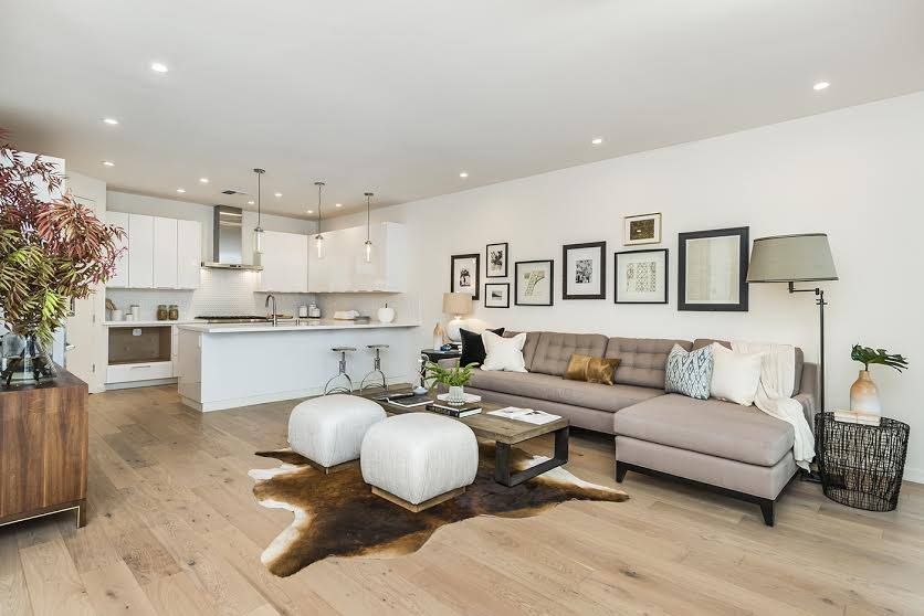 Bright modern living room with a beige sofa, white ottomans, gallery wall, and open kitchen in the background