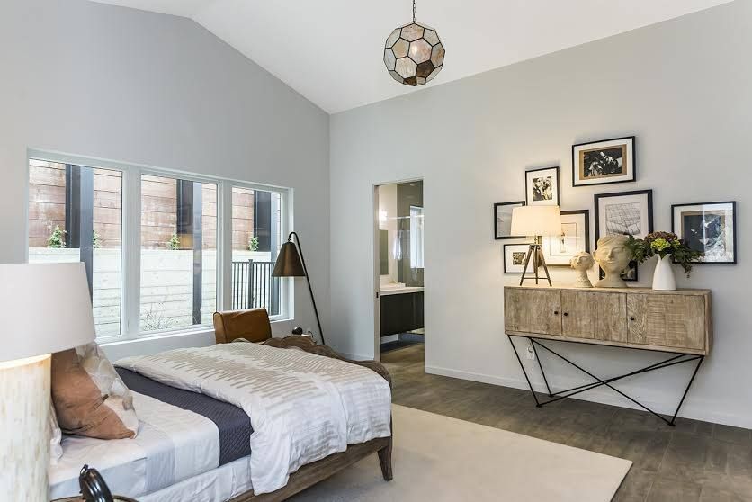Bright bedroom with a bed, gray walls, windows, and a wooden console with framed art.