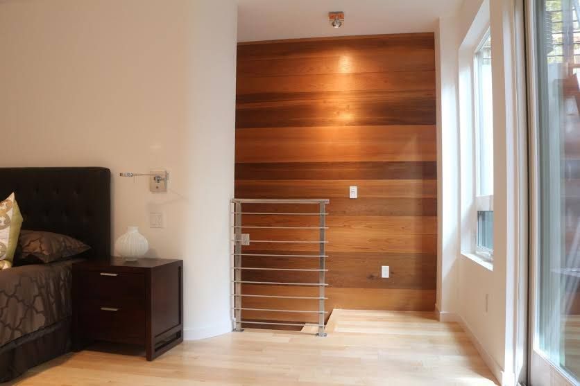Modern bedroom with wood accent wall, bed, nightstand, and large window on the right.