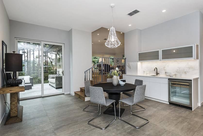 Modern open-concept kitchen and dining area with white cabinets, dark table, gray chairs, and sliding glass doors