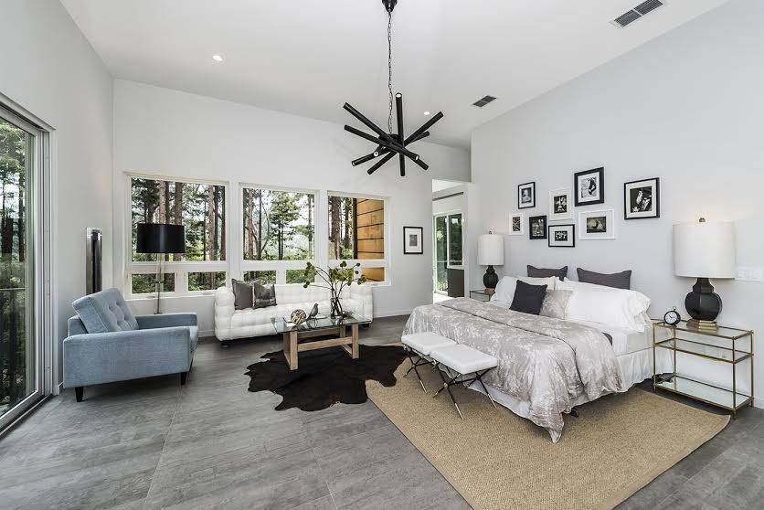Bright modern bedroom with gray carpet, white walls, black starburst chandelier, and a seating nook by large windows