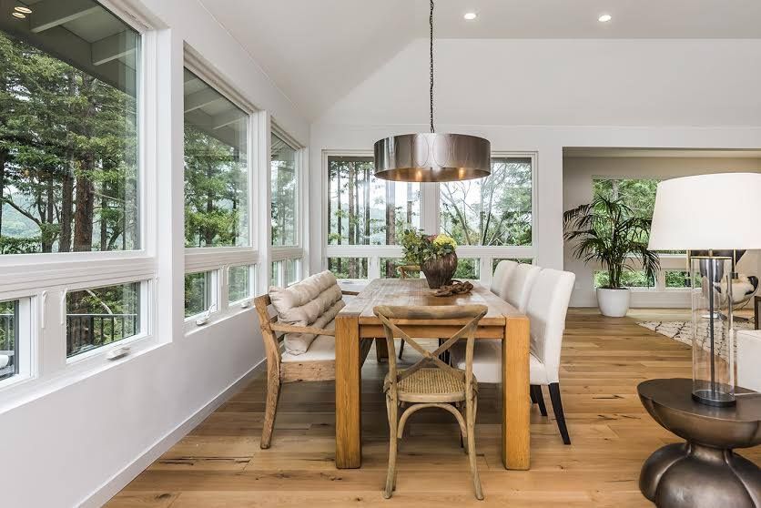 Bright dining room with wooden table, woven chairs, large windows, and a floor lamp