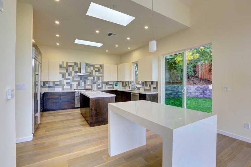 Bright modern kitchen with island, light wood floors, and large sliding glass doors to a green yard