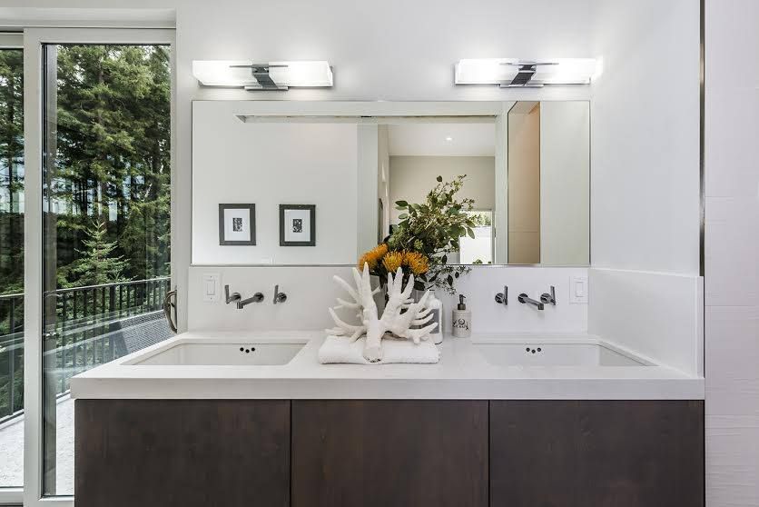 Modern bathroom vanity with double sinks, large mirror, wall lights, and a vase of flowers.