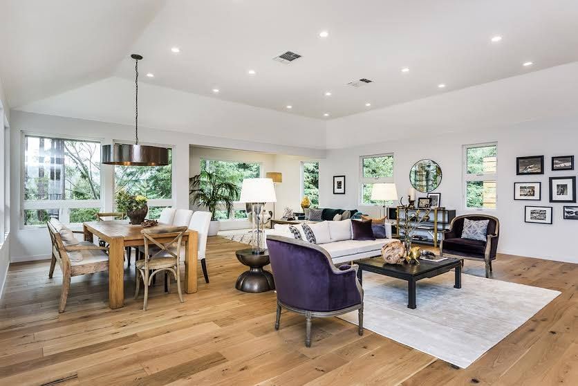 Bright open-plan living and dining room with wood floors, purple chairs, white sofa, and large windows