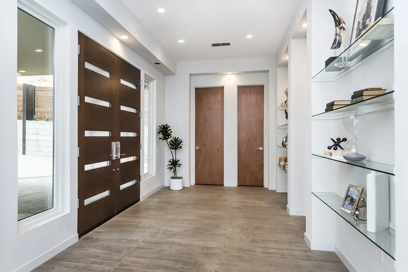 Modern hallway with wood doors, white walls, glass display shelves, and light wood flooring.
