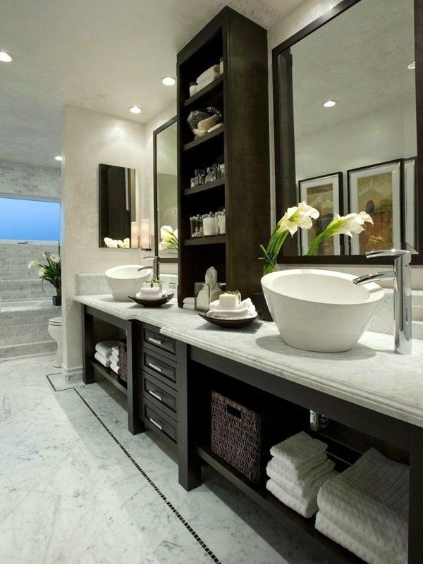 Modern bathroom vanity with dual sinks, white countertops, dark wood cabinets, and a large mirror in a bright room