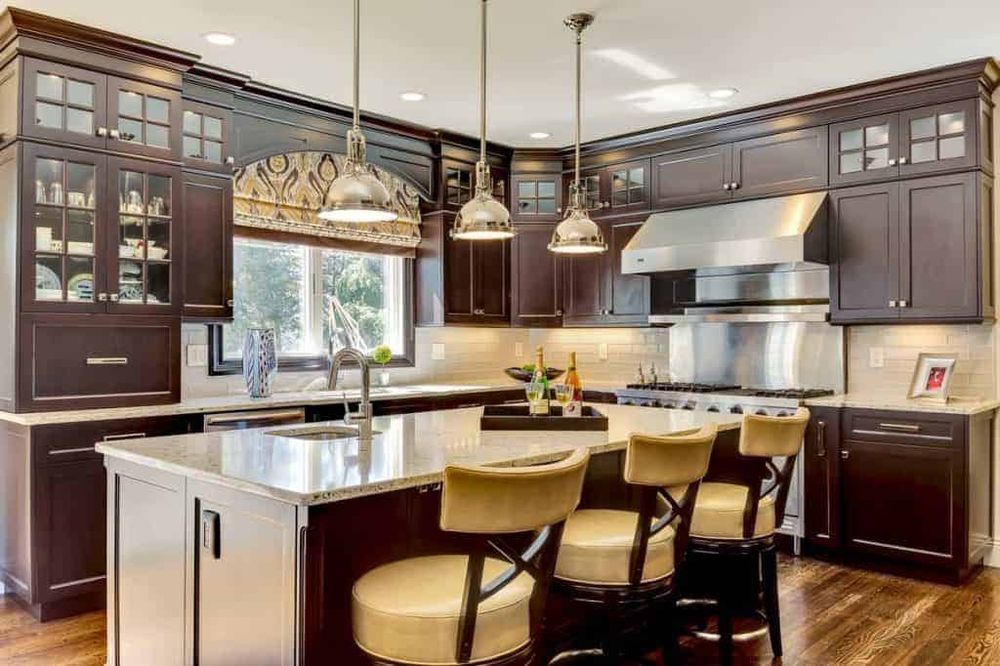 Modern kitchen with dark wood cabinets, large island, pendant lights, and stainless steel appliances