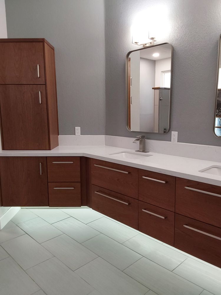 Modern bathroom vanity with brown cabinets, white countertop, mirror, and wall lights