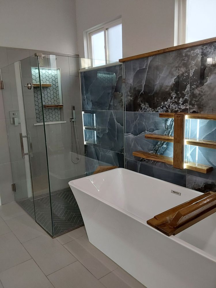 Modern bathroom with glass shower, white tub, and dark tile accent wall with shelves.