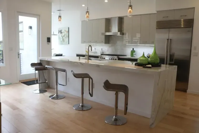 Modern kitchen with white island, three stools, stainless appliances, and hanging pendant lights