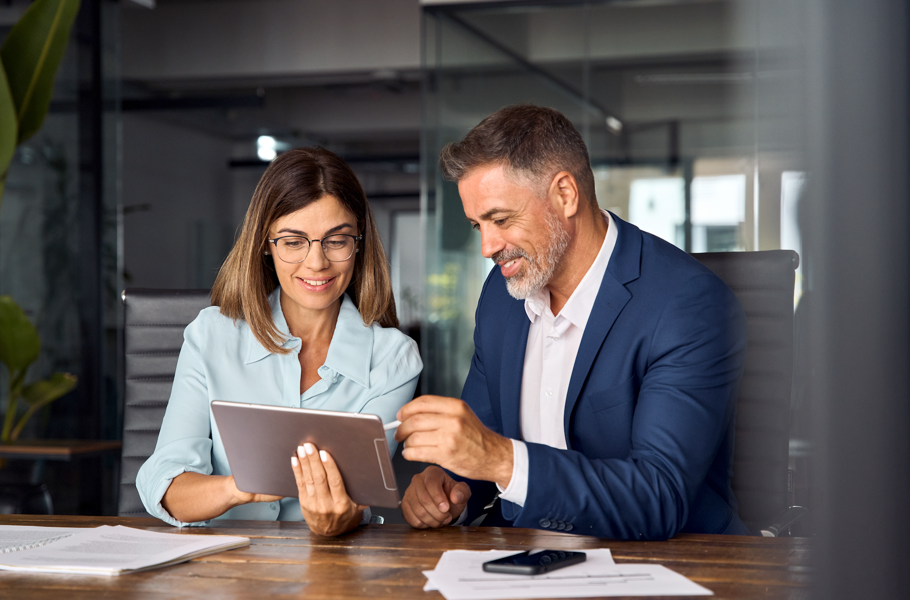 A man and a woman are sitting at a table looking at a tablet.