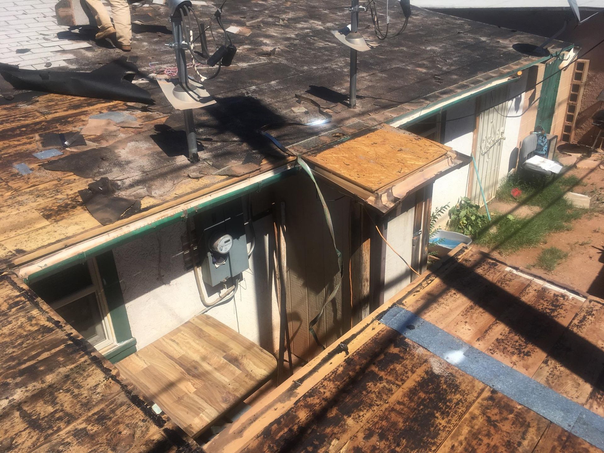 A high-angle view of a house roof under renovation, showing exposed wooden decking, dark roofing material, and a chimney.