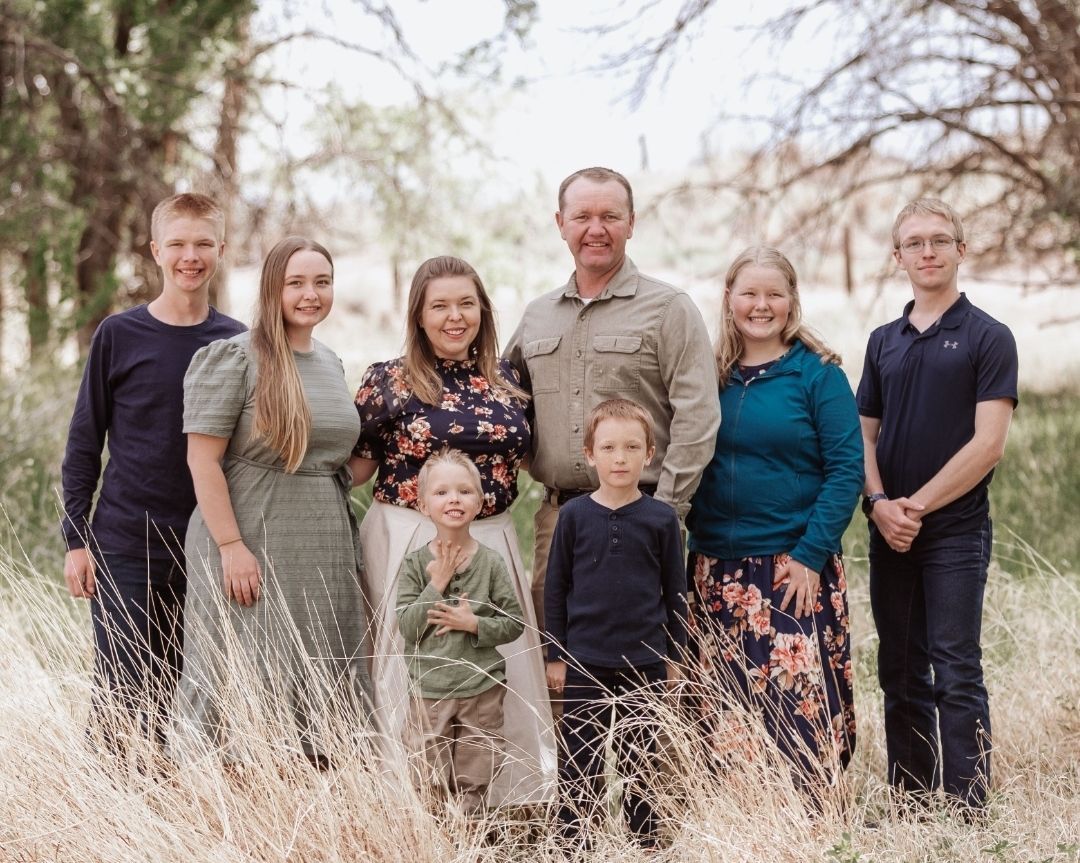 A group of eight people posing together in a grassy outdoor field, smiling for a photograph.