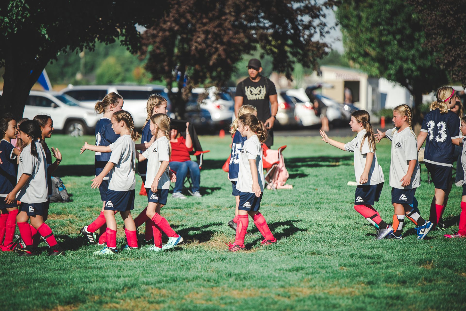 Children in soccer uniforms walking on a grassy field during a game