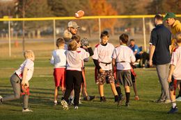 Coach kneels with children on a grassy field during an outdoor sports practice.