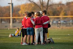 Coach instructing two children on a grassy field while others play in the background