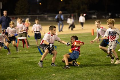 Child kicking an orange ball on a grassy field at an outdoor gathering