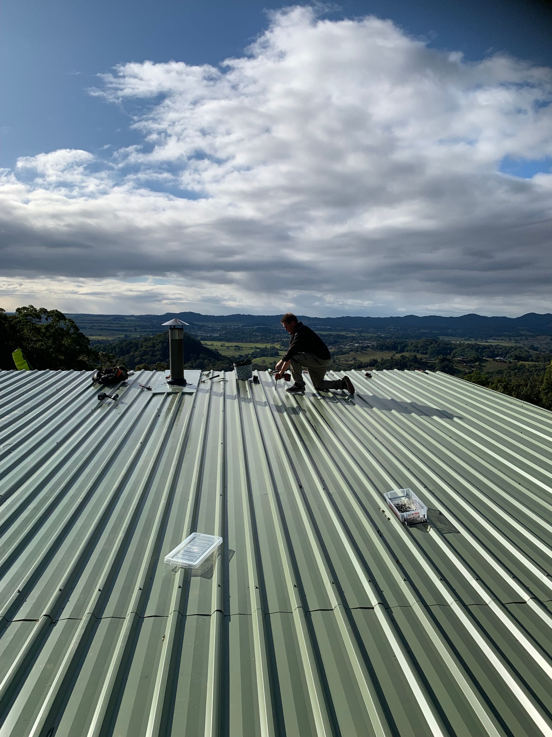 A man is kneeling down on a green metal roof — Blue Sky Roofing NSW In Murwillumbah, NSW