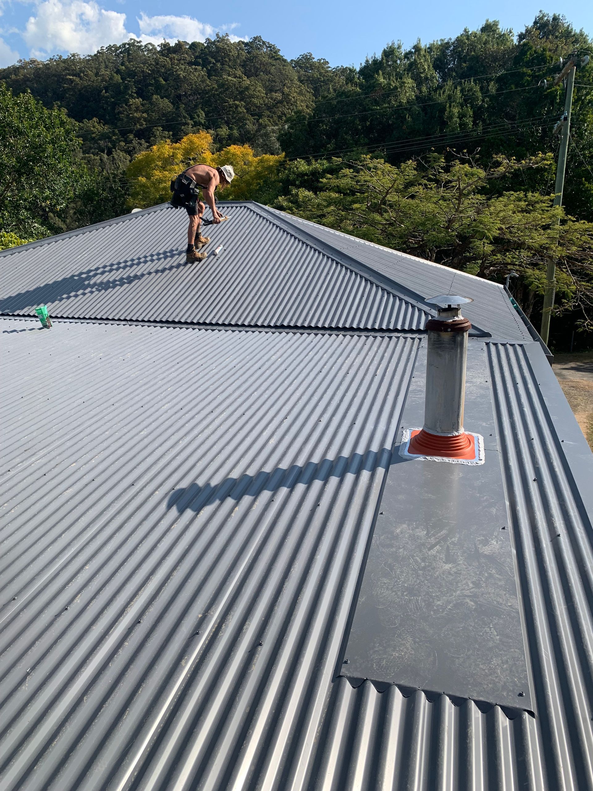 A navy blue roof with a worker on top doing repairs — Blue Sky Roofing NSW In Ocean Shores, NSW