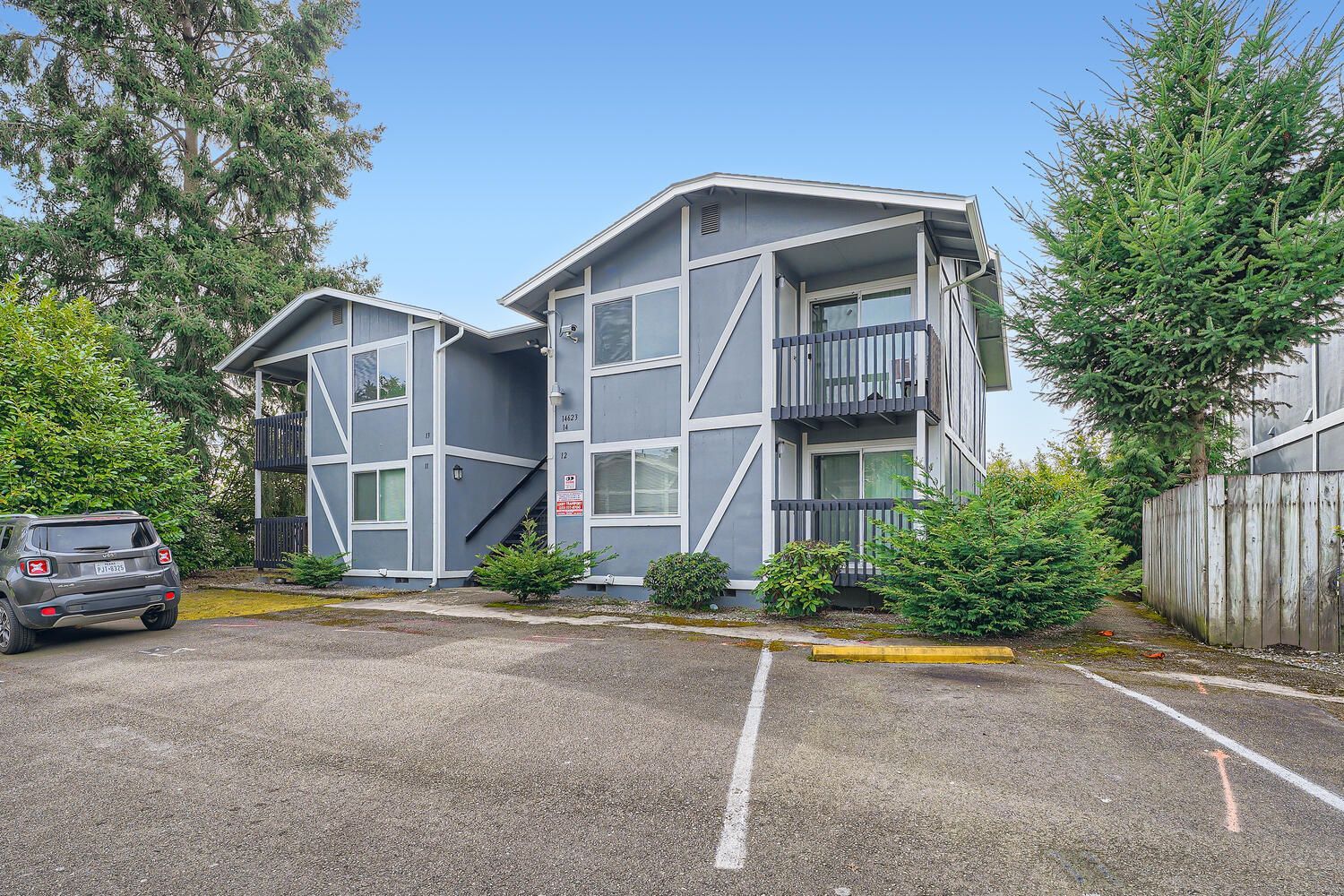 Photo showing a set of apartment buildings, with a parking lot and plenty of trees and bushes